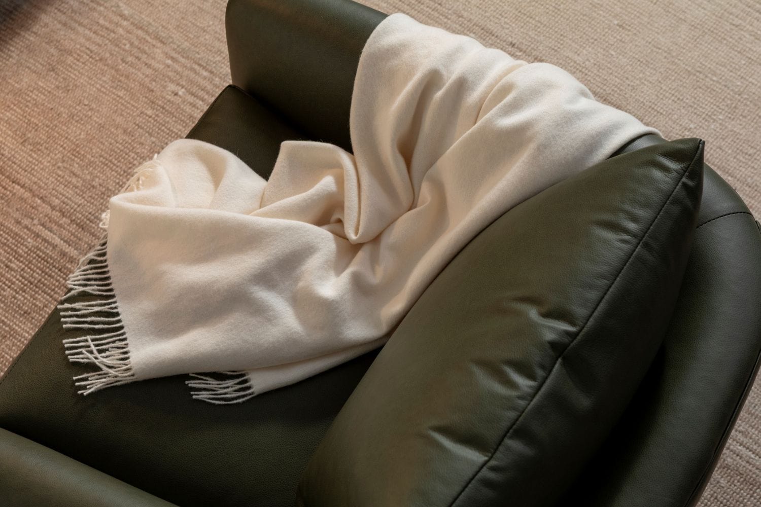 A forest green leather chair at a high angle with cream fabric throw draped over the arm