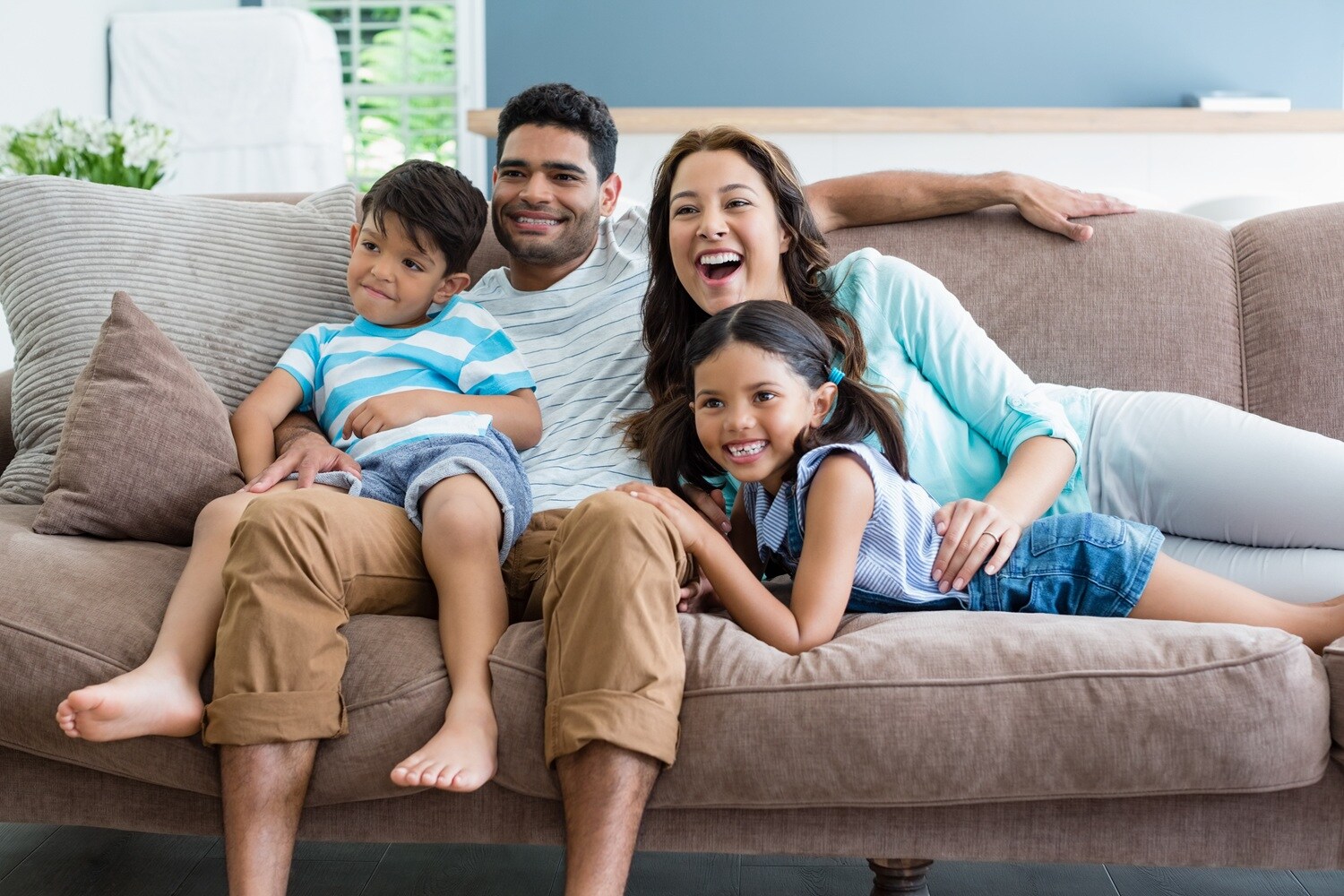 A family of four sitting and laughing on a brown sofa