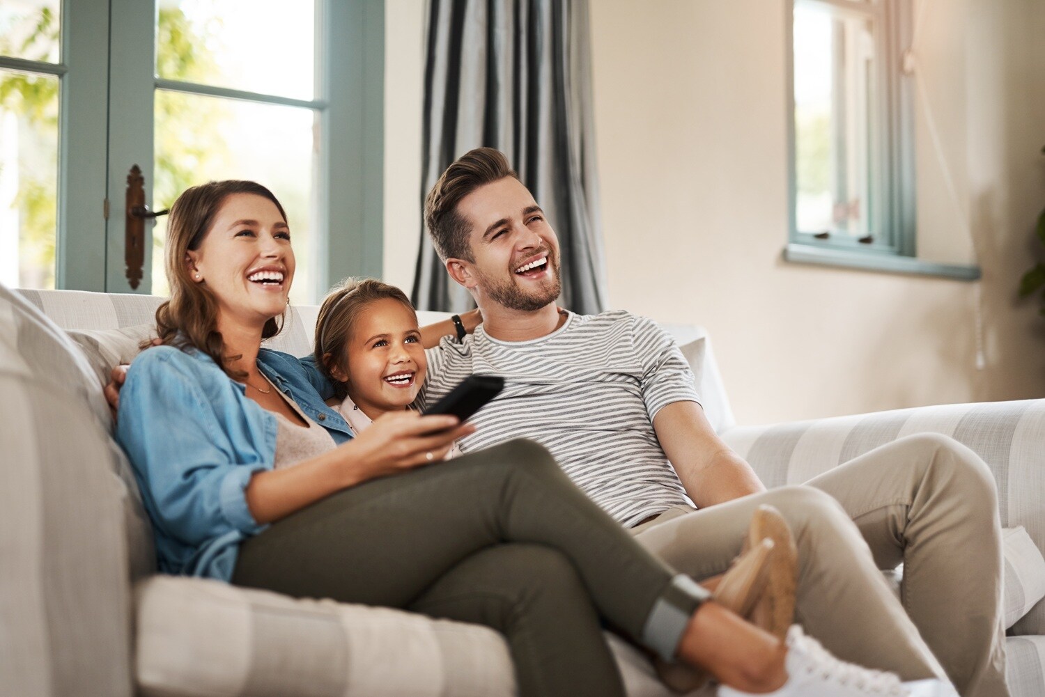 A family of three smiling on the sofa and watching TV